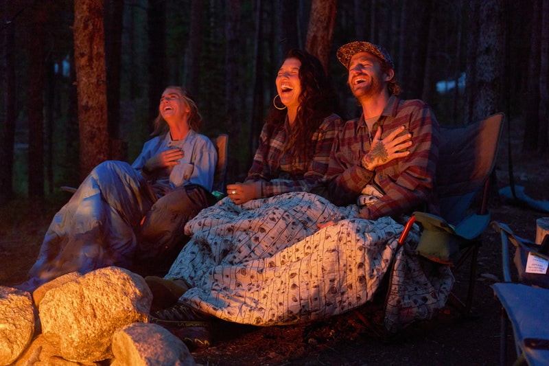 3 People sat on chairs near a campfire with Kelty Blankets